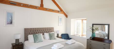 A bedroom with a large bed, a nightstand, a dresser, and a window with curtains.