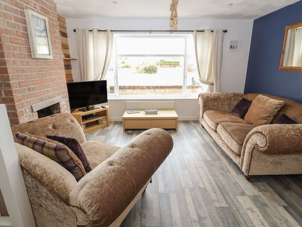 A living room with two sofas, a TV, a coffee table, and a brick wall.