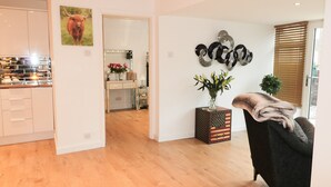A modern living room with a wooden floor, a black armchair, a decorative vase with flowers, and a vintage suitcase. - Swale Cottage (Chathill)