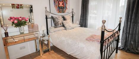 A bedroom with a bed, bedside table, mirror, and a decorative wall piece.