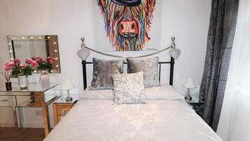 A bedroom with a bed, a vanity with a mirror, and a colorful artwork on the wall.