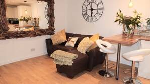 A modern living room with a brown leather sofa, a wooden coffee table, a white bar stool, a large mirror, and a wall clock. - Swale Cottage (Chathill)