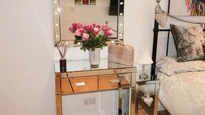 A vanity with a mirror, a vase of pink flowers, a decorative lamp, and a small jewelry box. - Swale Cottage (Chathill)