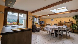 Ein gemütliches Wohnzimmer mit Essbereich, Holzbalken, einem Fernseher und einem großen Fenster mit Blick auf Grünflächen.