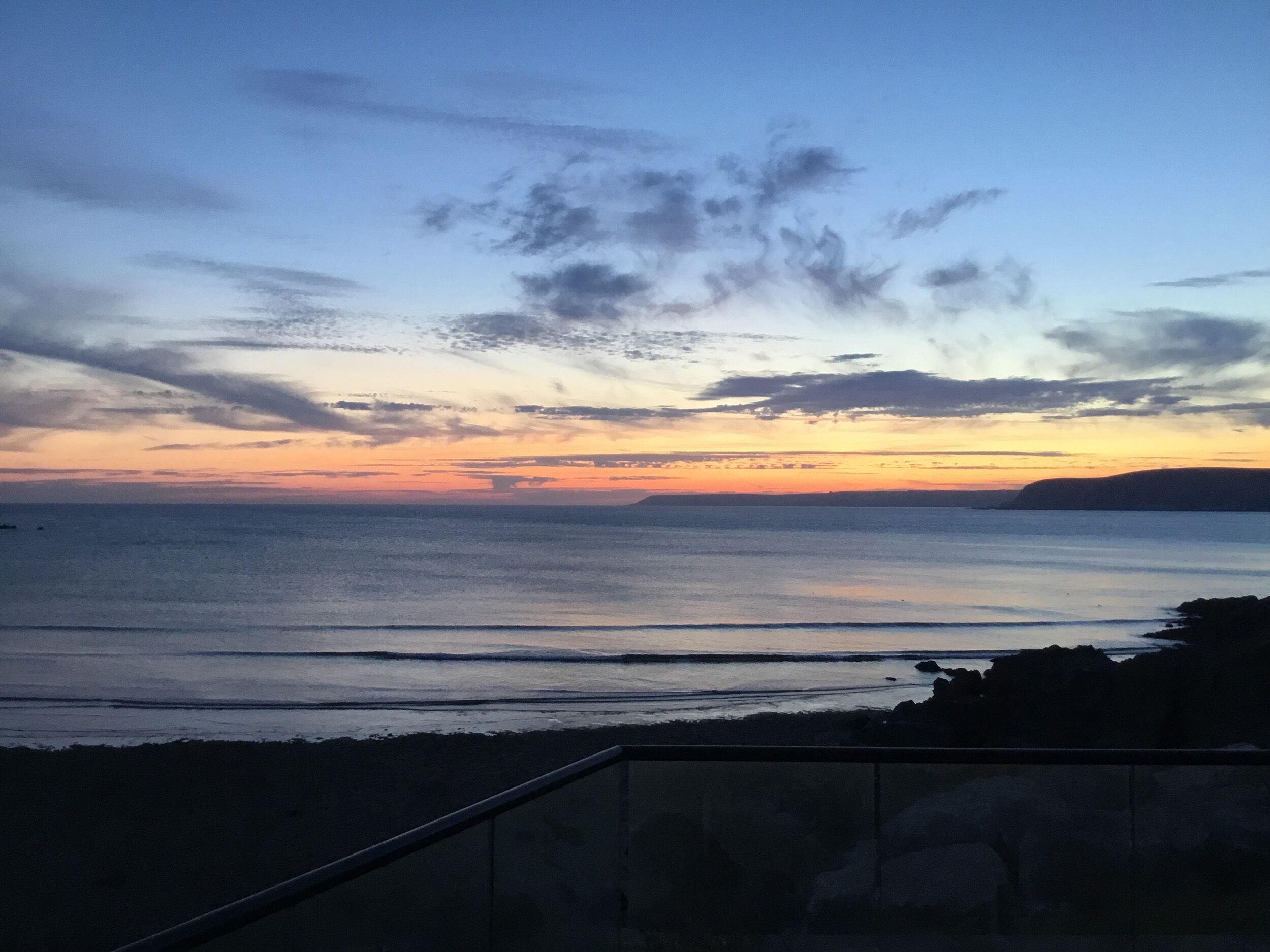 A coastal sunset view with a railing in the foreground.