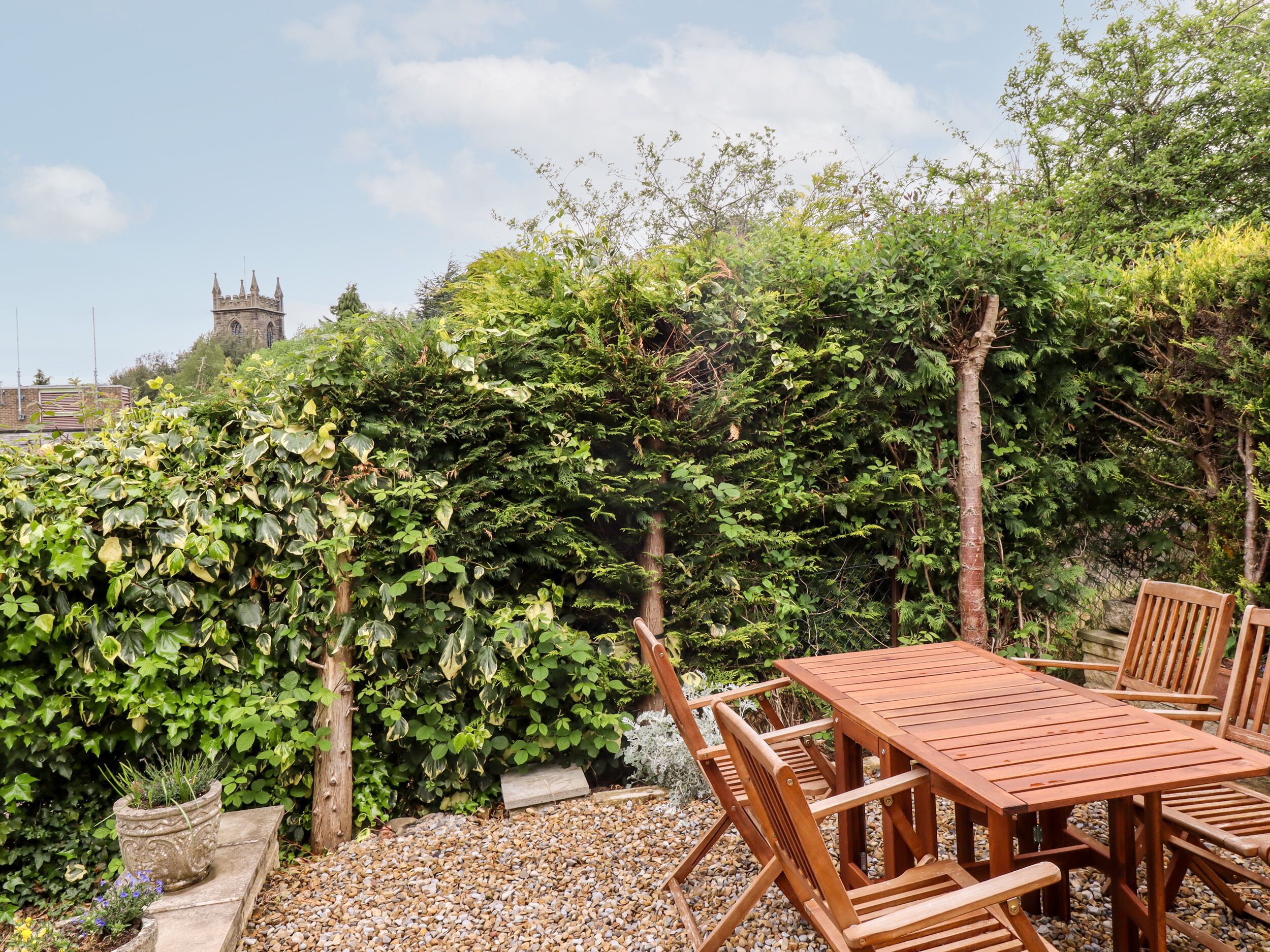 A wooden table and chairs set in a garden with a stone wall and greenery.
