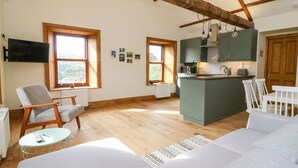 Una sala acogedora con sofá, una silla, una mesita y una cocina con encimera y alacenas.
