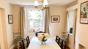 A dining room with a long table, six chairs, a chandelier, a window with curtains, and framed pictures on the walls. - Fell Foot (Holmrook)
