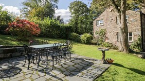A stone house with a stone patio, a table with chairs, and a tree. - Fell Foot (Holmrook)