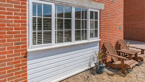 A brick house with a large white-framed window, a small garden with a potted plant, and wooden outdoor furniture. - 26 Burtons Mill (Norwich)