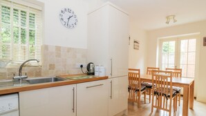 A modern kitchen with white cabinets, a stainless steel sink, and a coffee machine. There is a dining area with wooden chairs and a table. - 26 Burtons Mill (Norwich)