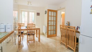 A modern kitchen with wooden furniture, a white refrigerator, and a dining area with chairs and a table. - 26 Burtons Mill (Norwich)