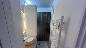 Un baño compacto con un lavabo blanco, cabina de ducha de vidrio y un perchero blanco.