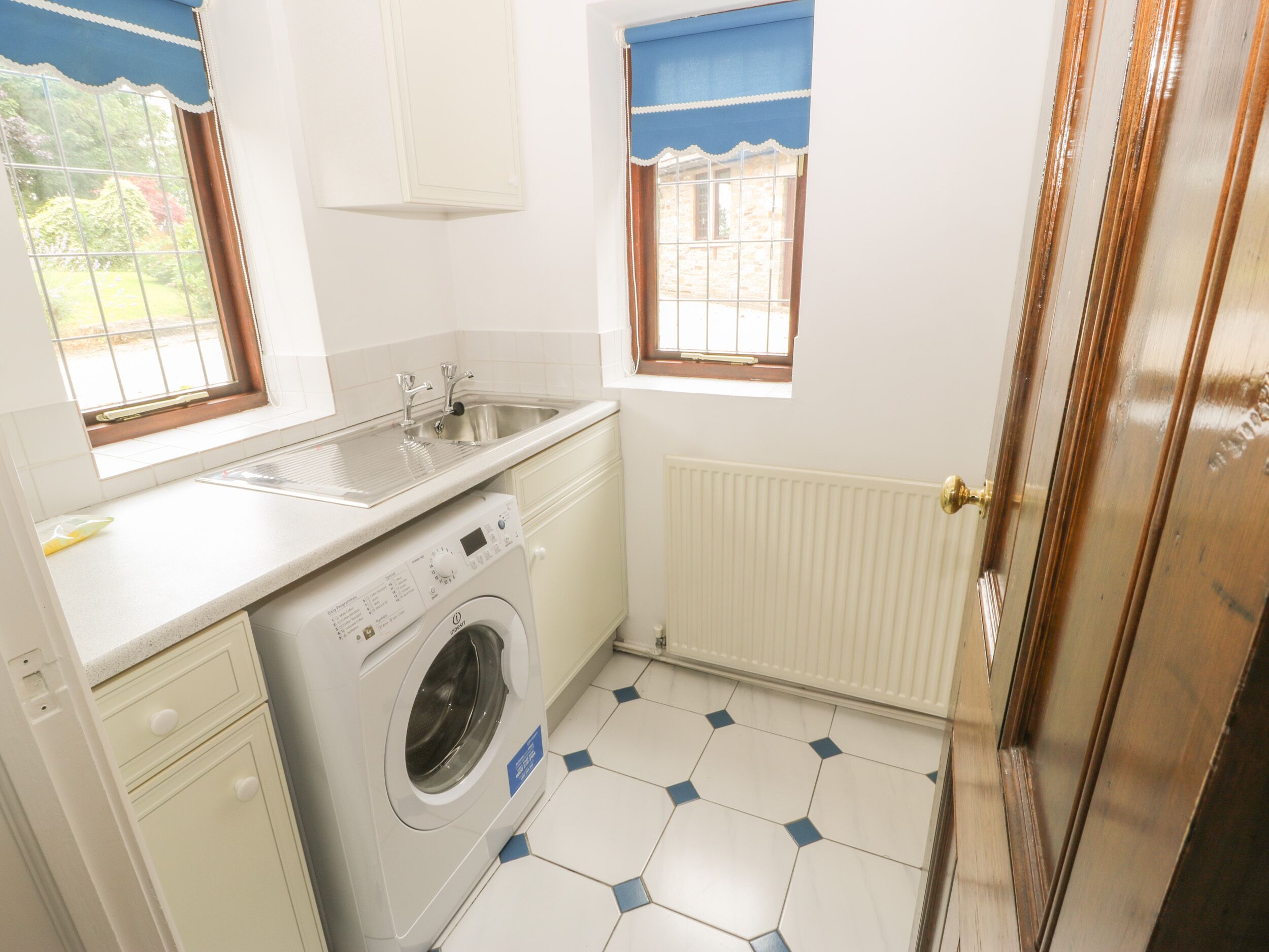 Cocina compacta con lavadora integrada, un lavamanos y una ventana con cortina azul.