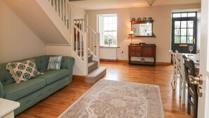 A living room with a green sofa, a wooden staircase, a dining area with a table and chairs, and a large window with a view. - Ballintlea (Knockanroe)