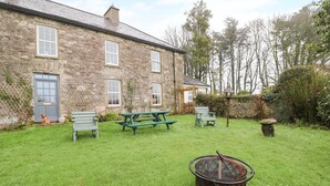 A stone building with a door, windows, and a small garden area with a fire pit. - Ballintlea (Knockanroe)