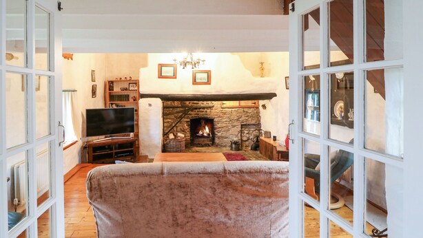 A cozy living room with a stone fireplace, wooden flooring, and a television. - Ballintlea (Knockanroe)