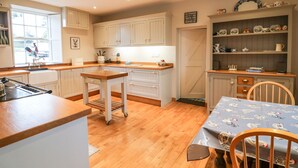 A kitchen with wooden cabinets, a sink, a stove, a table with chairs, and a shelf with dishes. - Ballintlea (Knockanroe)