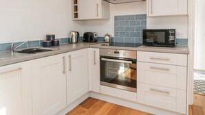 A modern kitchen with white cabinets, a black microwave, a kettle, and a stainless steel oven. - Old Kiln Cottage (Dumfries)