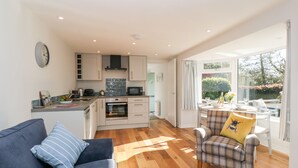 A modern kitchen with white cabinets, a microwave, and a toaster. There is a dining area with a table and chairs, and a sofa with a plaid cushion. - Old Kiln Cottage (Dumfries)