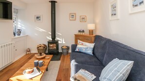 A cozy living room with a fireplace, a sofa, a coffee table with a book, and a window with a view of the outside. - Old Kiln Cottage (Dumfries)