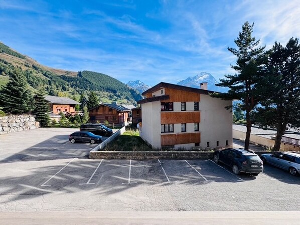 Un edificio moderno con estacionamiento, rodeado de montañas y árboles.