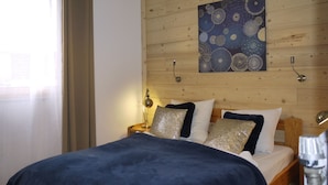Ett sovrum med en sänggavel i trä, en säng med ett blått överkast och dekorativa kuddar, ett konstverk som hänger på väggen och sänglampor.