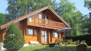 A wooden cabin with a balcony, a bench, and a potted plant in the yard. - Comfortable chalet in Cleurie with WIFI, fireplace, and terrace (Cleurie)