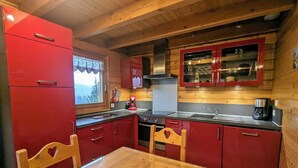 A compact kitchen with red cabinetry, a wooden dining table, and a window with a view. - Comfortable chalet in Cleurie with WIFI, fireplace, and terrace (Cleurie)