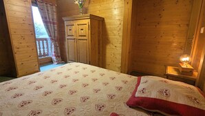A wooden cabin bedroom with a bed, a nightstand, a dresser, and a window with curtains. - Comfortable chalet in Cleurie with WIFI, fireplace, and terrace (Cleurie)