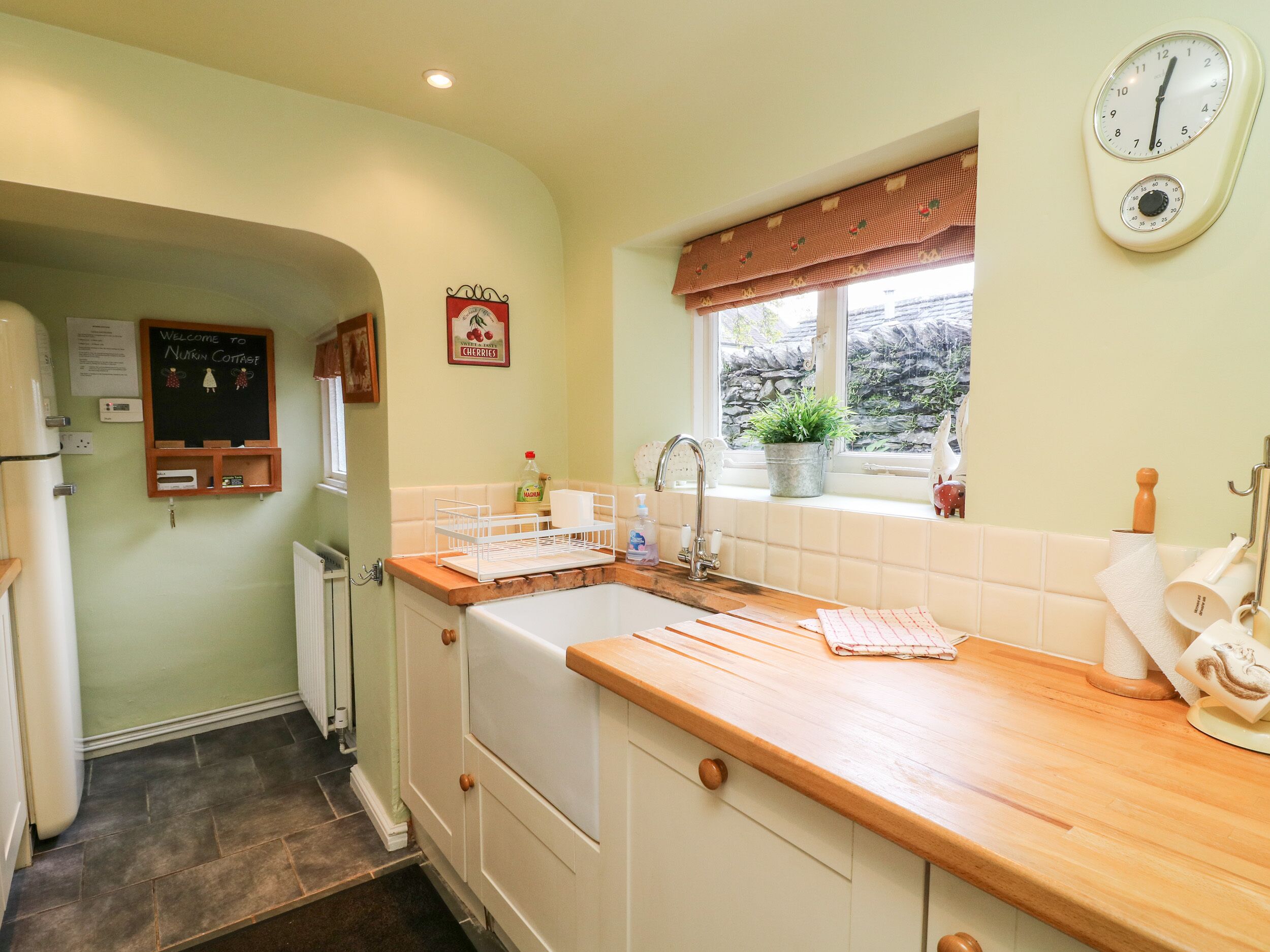 A kitchen with a wooden countertop, a sink, a window with a view, and a wall clock.