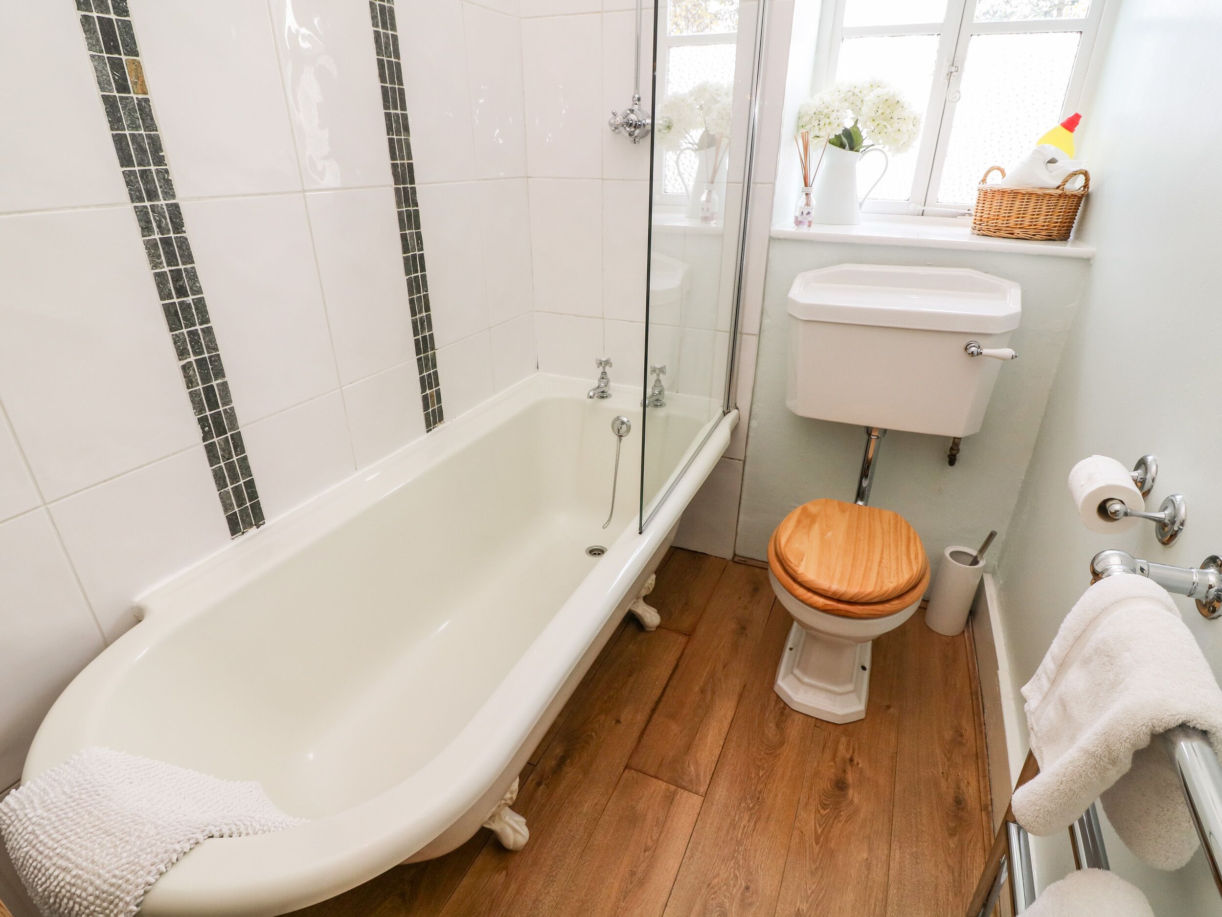 Un baño con bañera, inodoro y ventana con flores.