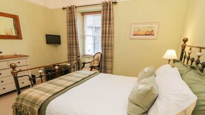Ein Schlafzimmer mit Bett, Schminktisch, Stuhl, einem Fenster mit Vorhängen, einem Gemälde und einer Lampe.