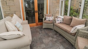 Un patio acogedor con pared de piedra, puerta de madera, mobiliario de mimbre y vistas al exterior.