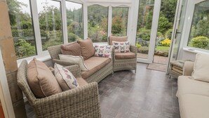Un solarium con mobiliario de mimbre, ventanas amplias y vistas a un jardín.