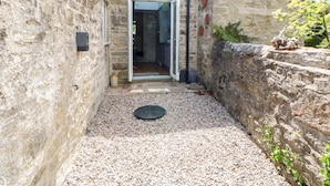 A narrow stone pathway leading to a doorway, with a small garden area and a stone wall on one side. - Hawthorne Cottage (Barnard Castle)
