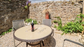 A round table with a bottle of wine and glasses, set against a stone wall with greenery. - Hawthorne Cottage (Barnard Castle)