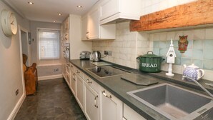A kitchen with white cabinets, a black countertop, a green pot labeled 'BREAD', a white birdhouse, and a blue and white teapot. - Millstream Cottage (Hope Valley)