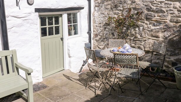 A stone wall, a white door, and a table with chairs in a courtyard. - Millstream Cottage (Hope Valley)