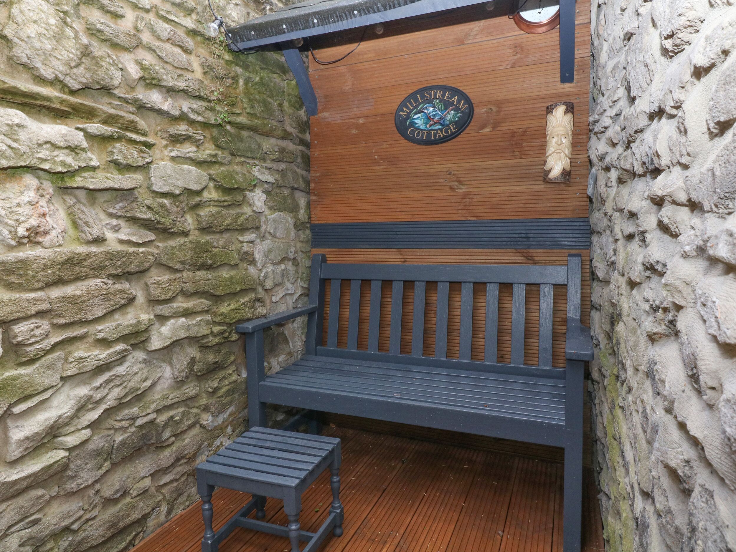 A wooden bench with a metal frame, a small stool, and a stone wall.