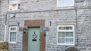 A stone building with a green door, a heart-shaped decoration, and a sign reading "Millstreet Cottage." - Millstream Cottage (Hope Valley)
