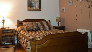 A bedroom with a wooden bed, a nightstand, a lamp, a wall-mounted picture, and a decorative wall hanging.