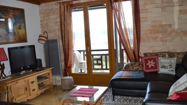 A cozy living room with a television, wooden furniture, a glass table, and a sofa with decorative pillows.