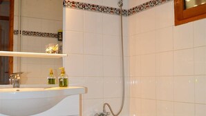 A bathroom with a white sink, a mirror, a shower, and a tiled wall.