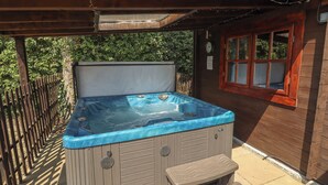 A hot tub with a wooden exterior, a wooden deck, and a window with a red frame.