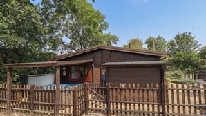 A wooden cabin with a fenced area, a small shed, and a clear sky.