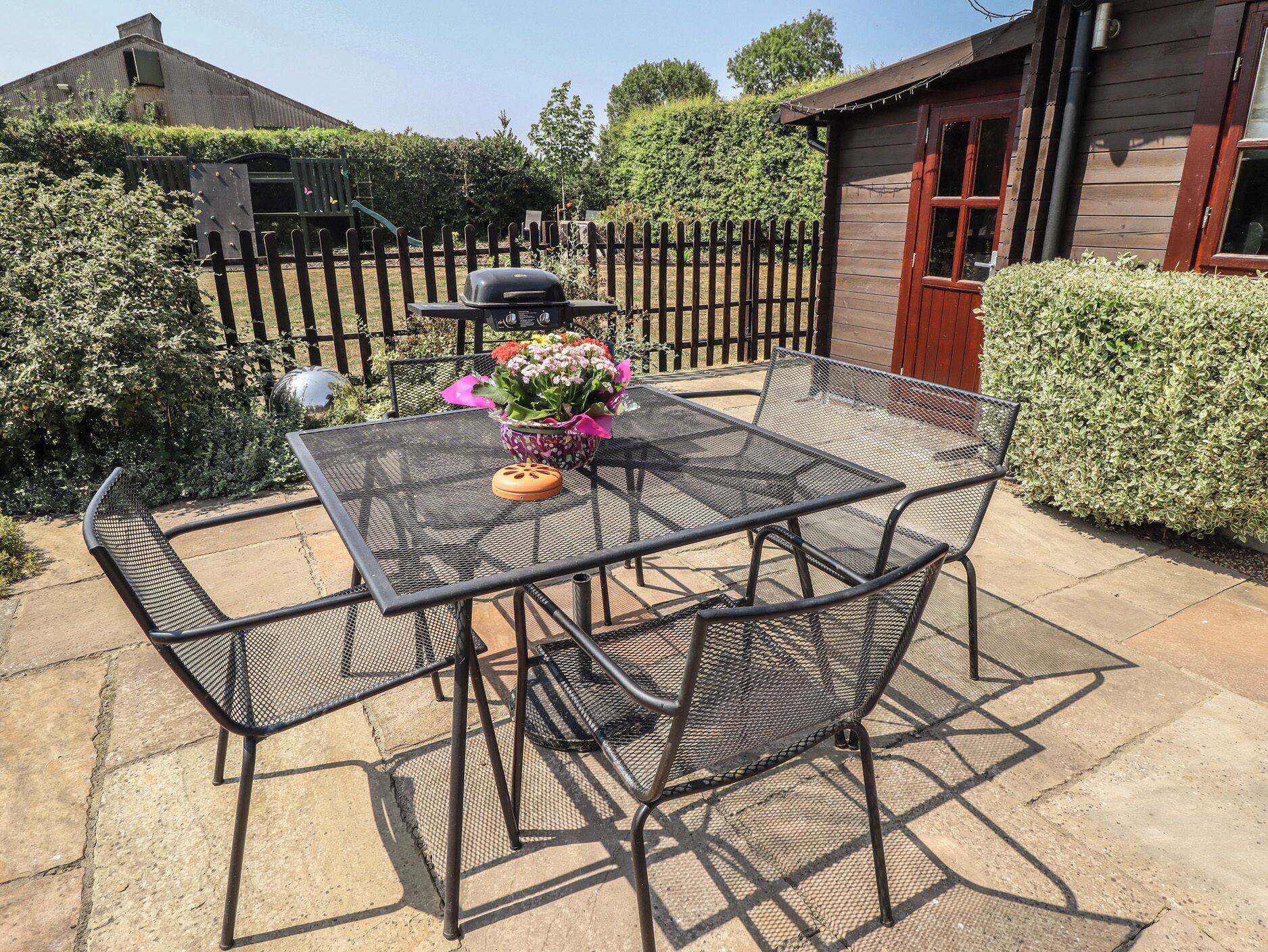A metal table and chairs set on a patio with a garden in the background.