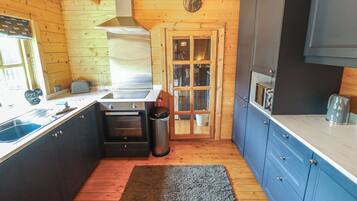 Eine kleine Küche mit Holzwänden, einem Edelstahl-Spülbecken, einem eingebauten Backofen und blauen Schränken.