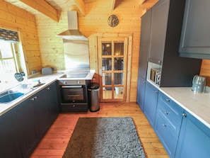 A compact kitchen with wooden walls, a stainless steel sink, a built-in oven, and blue cabinets. - Tythe Lodge Hot Tub Retreat in Rural Lincolnshire Family-friendly Lodge Near Heckington (Sleaford)
