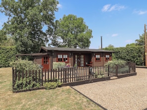 A wooden cabin with a gravel driveway, surrounded by a wooden fence and greenery. - Tythe Lodge Hot Tub Retreat in Rural Lincolnshire Family-friendly Lodge Near Heckington (Sleaford)